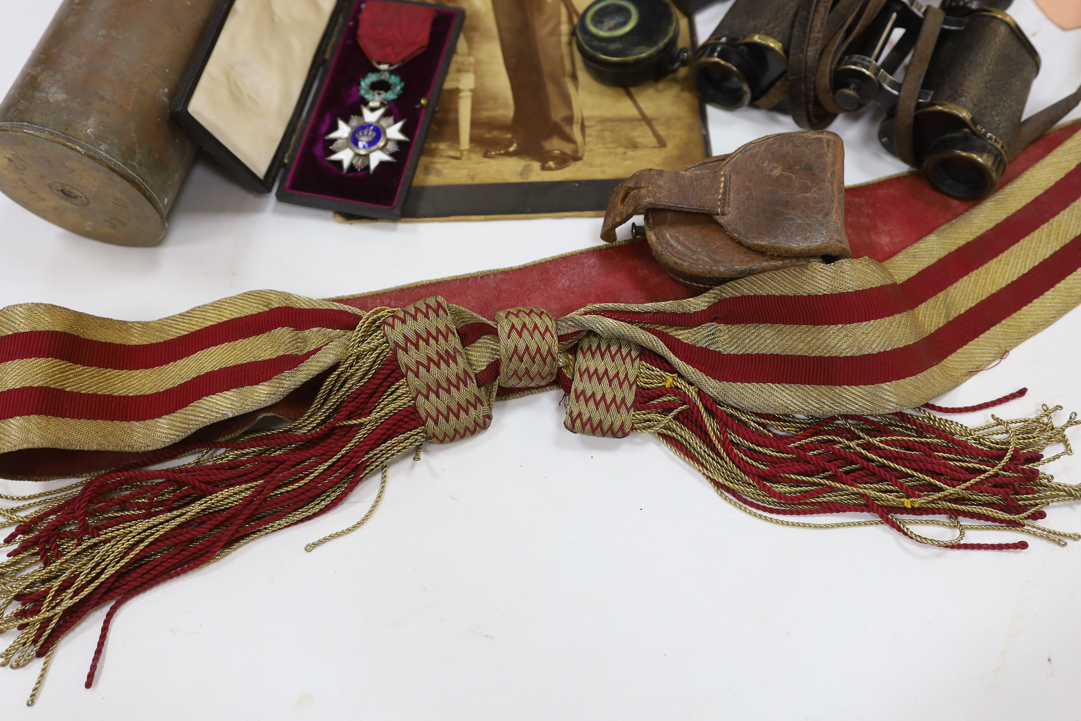 A late 19th century military sash with a related photograph showing the full uniform, a pair of Carl Zeiss binoculars, two compasses, a Belgium Order of the Crown cased medal, and a shell casing